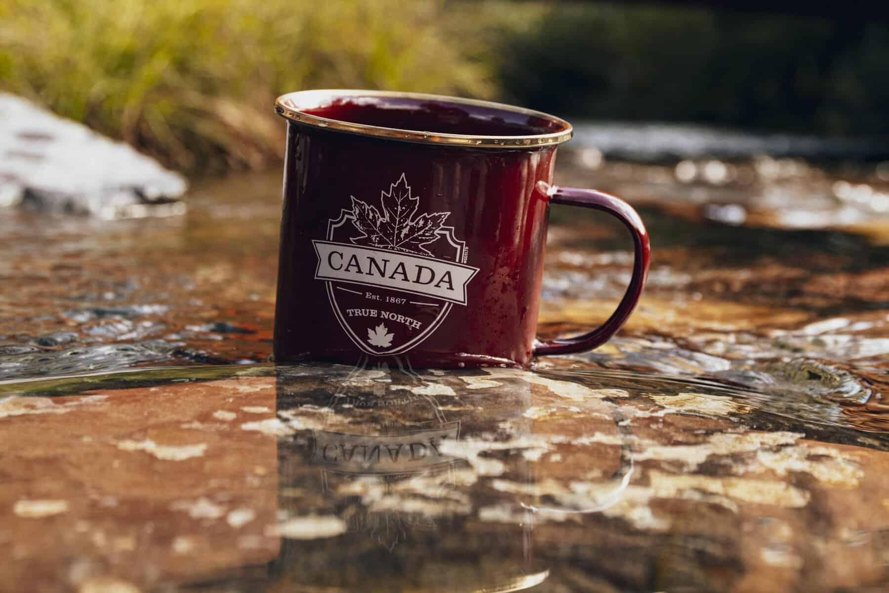 Red metal mug with Canada design placed in a river setting during fall.